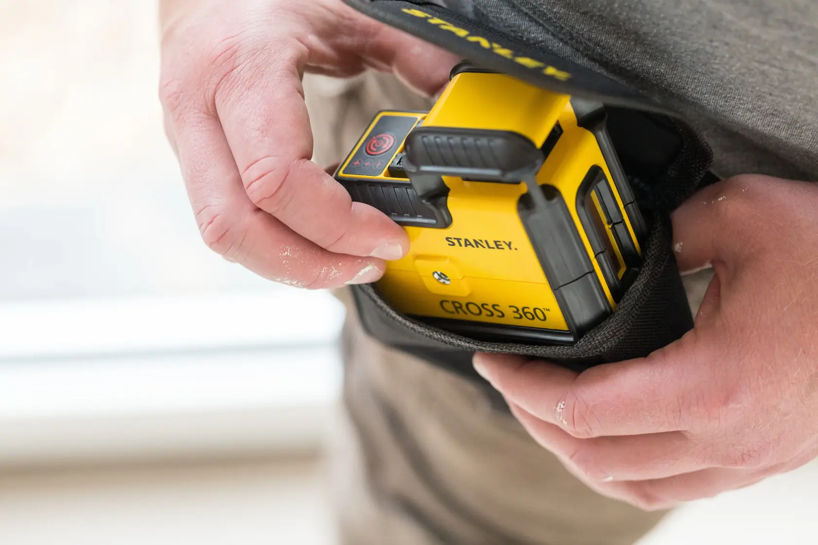 STANLEY STHT77504-1 yellow CROSS 360° laser level being placed into a black carrying pouch by hand.