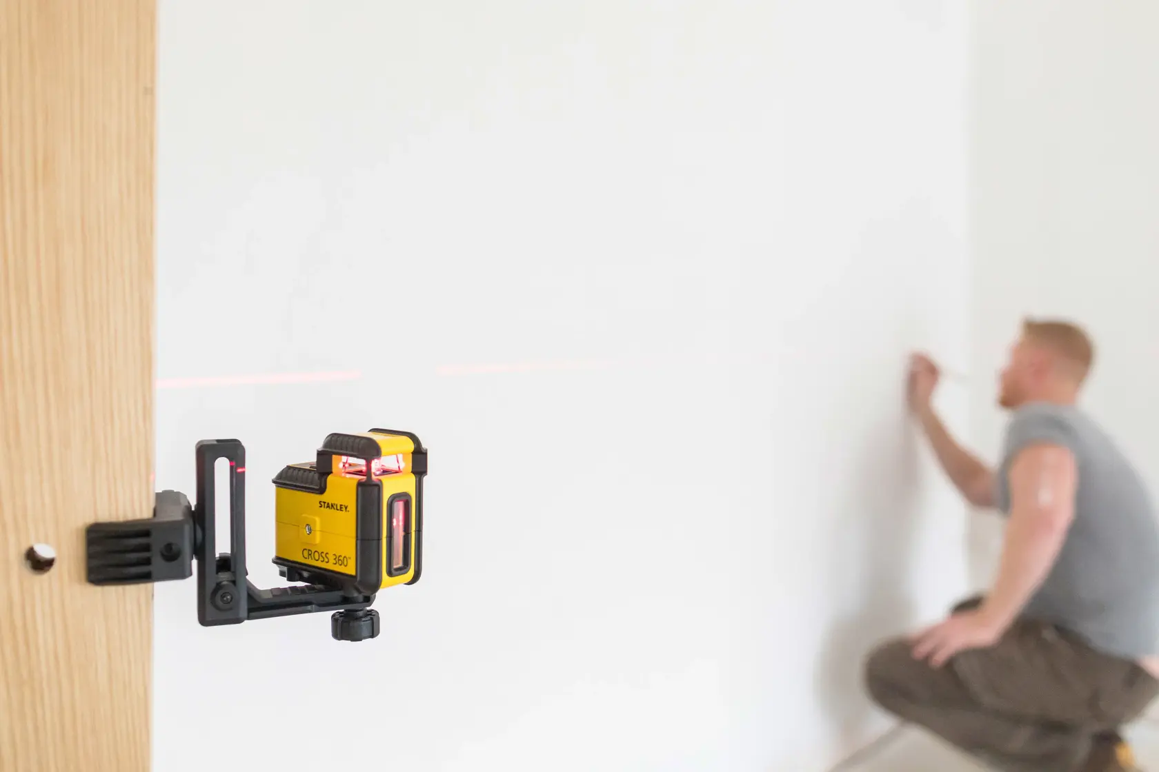 STANLEY STHT77504-1 laser level device mounted on wood, emitting red line, person marking wall.