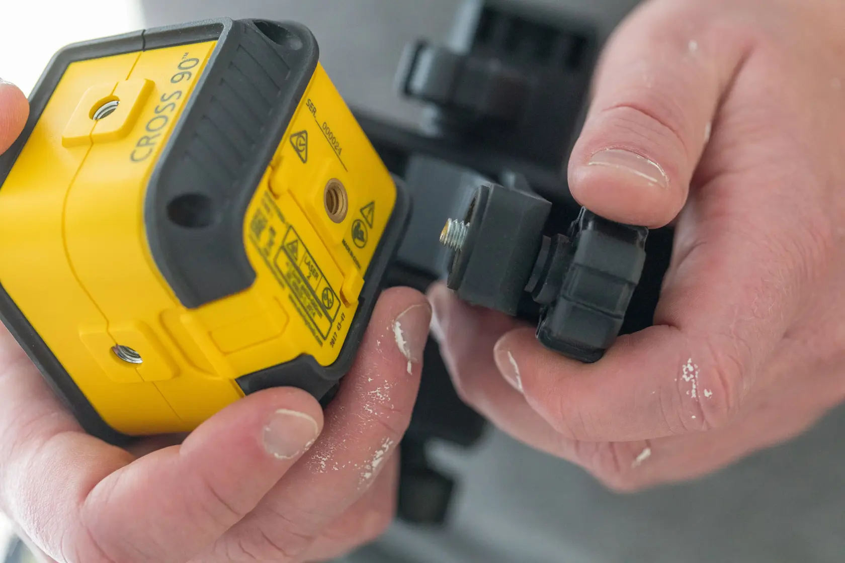 STANLEY STHT77592-1 yellow cross line laser level being attached to mounting bracket, close-up.