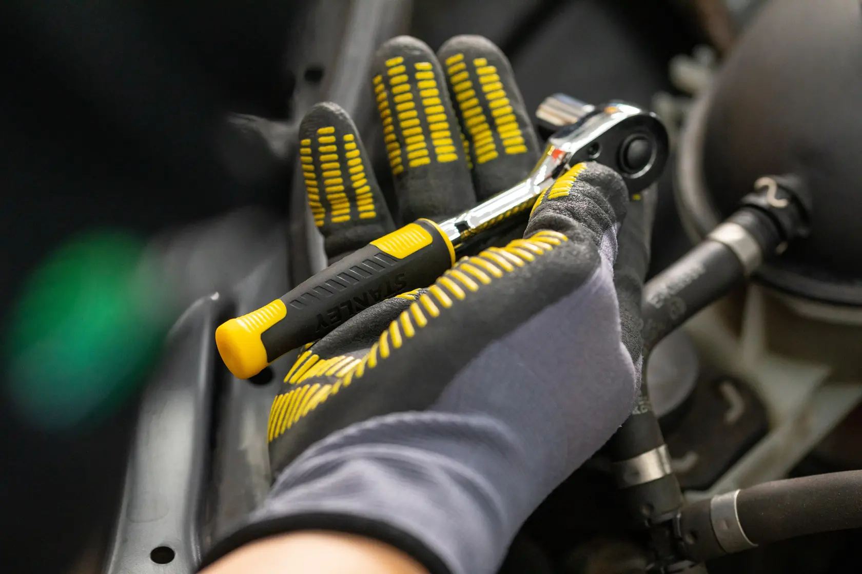 STANLEY STMT82832-1 ratchet with black and yellow grip held by gloved hand, closeup during automotive work.