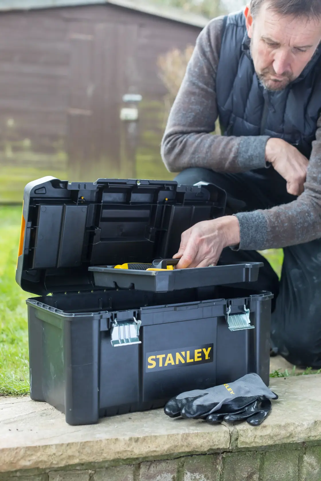 Photo of STANLEY STST1-75521 toolbox outdoors, lid open showing tray, gloves placed in front, person using it.