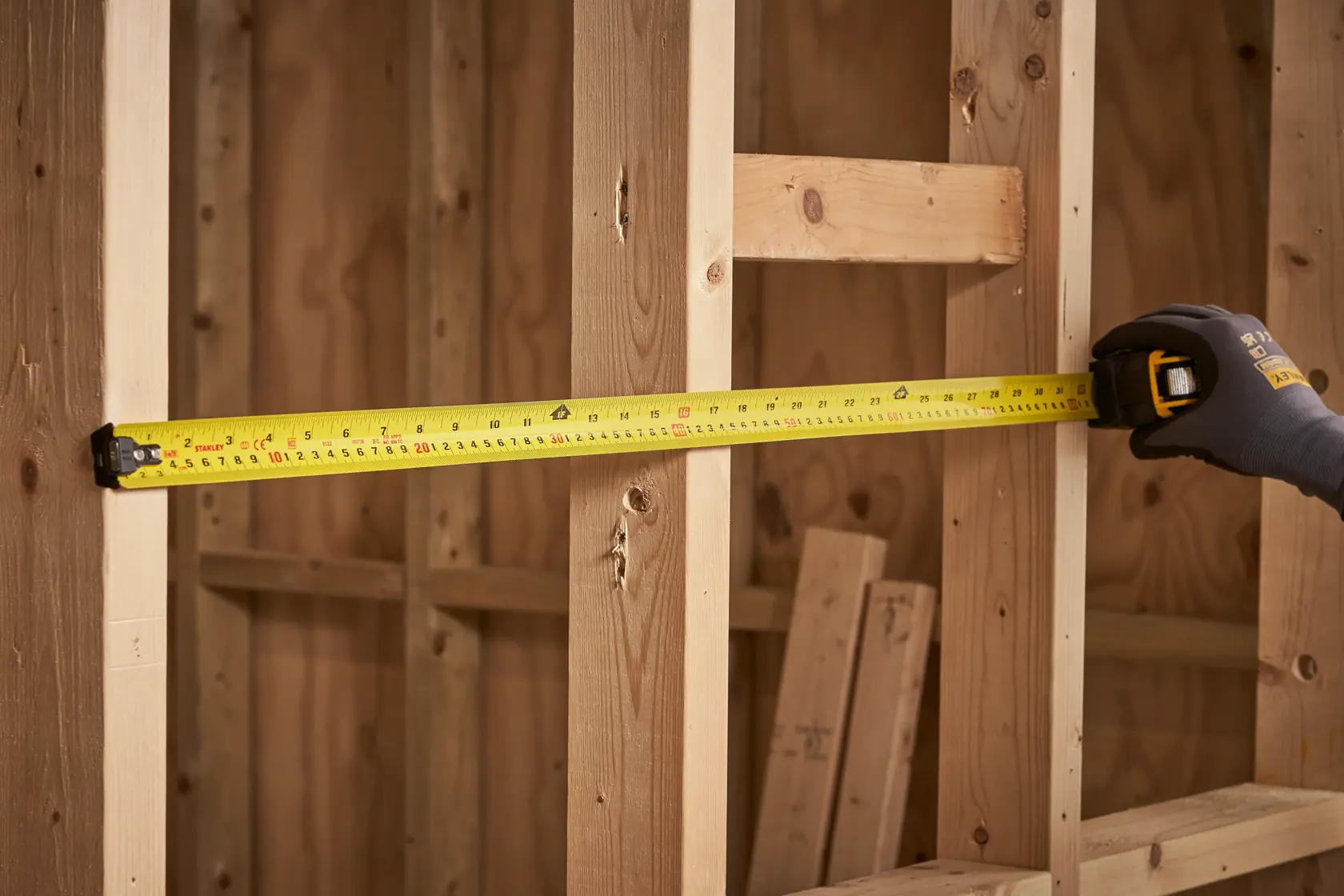 STANLEY XTHT0-33504 tape measure extended against wooden framing, angled view, construction setting.