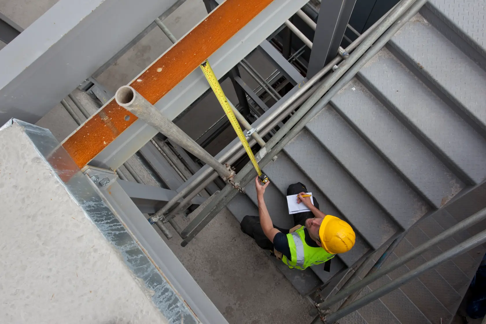 STANLEY XTHT0-33504 tape measure used by worker on stairs at construction site, viewed from above.